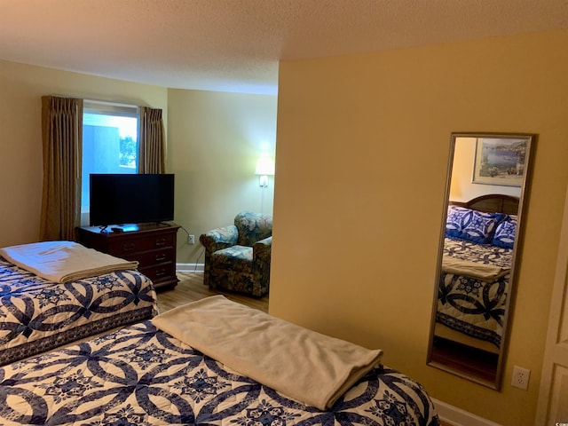 bedroom with a textured ceiling, light wood finished floors, and baseboards