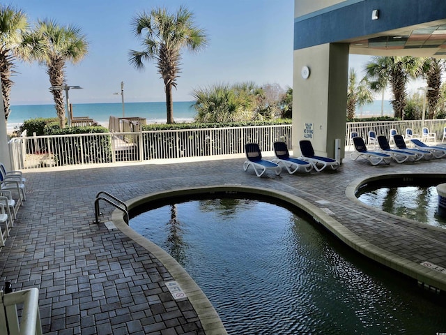 view of swimming pool featuring a water view, fence, a swimming pool, and a patio