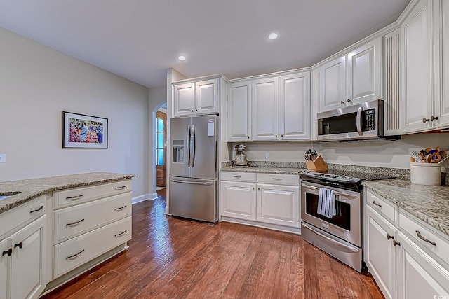 kitchen with white cabinets, stainless steel appliances, light stone countertops, and dark wood-type flooring