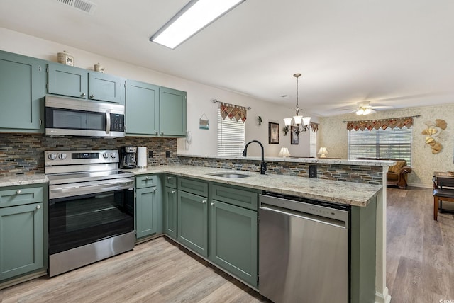 kitchen with pendant lighting, ceiling fan with notable chandelier, appliances with stainless steel finishes, light stone counters, and kitchen peninsula