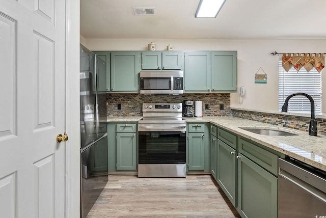 kitchen with backsplash, light stone counters, stainless steel appliances, sink, and green cabinetry