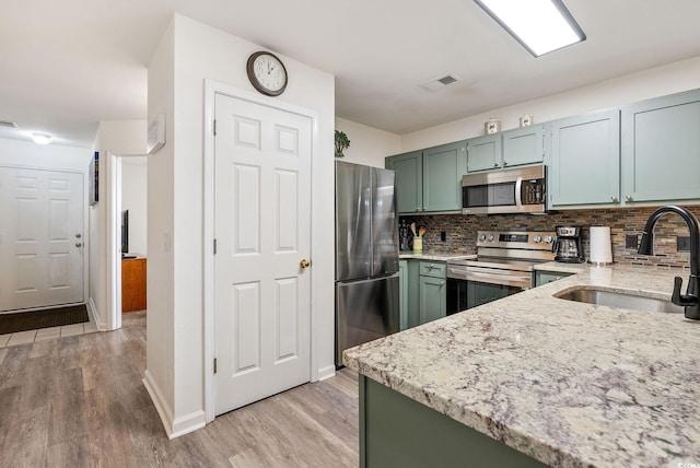 kitchen with light stone countertops, sink, stainless steel appliances, light hardwood / wood-style floors, and decorative backsplash