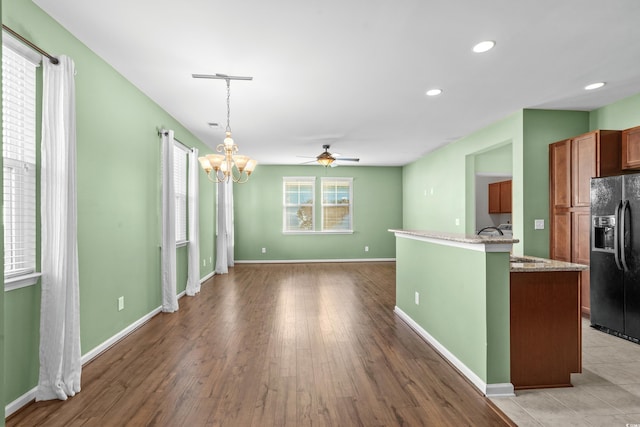 kitchen with black refrigerator with ice dispenser, ceiling fan with notable chandelier, sink, hardwood / wood-style flooring, and hanging light fixtures