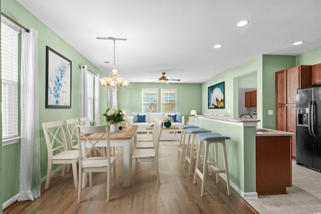 dining area with light wood-type flooring, ceiling fan with notable chandelier, and sink