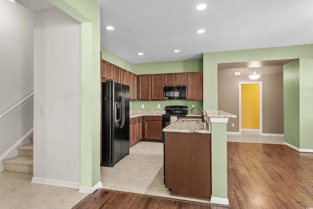 kitchen featuring kitchen peninsula, light stone counters, sink, black appliances, and light tile patterned flooring