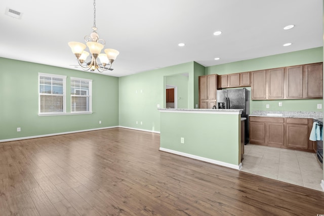 kitchen featuring black fridge, light hardwood / wood-style flooring, an inviting chandelier, a kitchen island, and hanging light fixtures