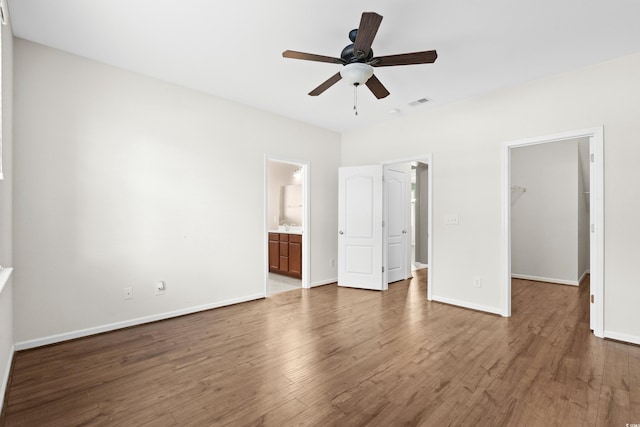 unfurnished bedroom featuring a walk in closet, ceiling fan, hardwood / wood-style flooring, connected bathroom, and a closet