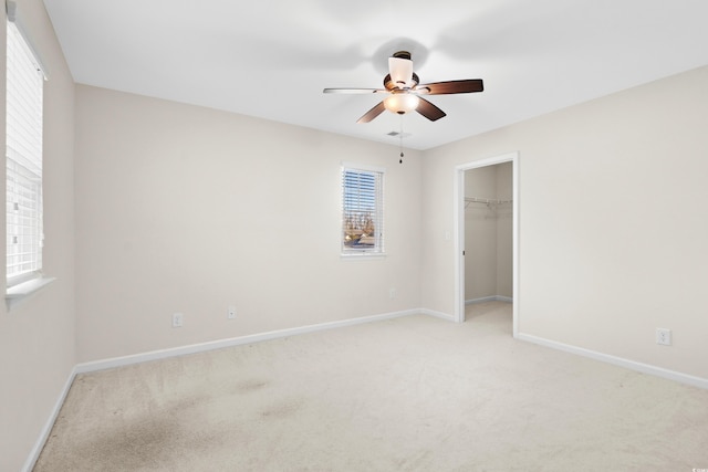 interior space with multiple windows, a walk in closet, light colored carpet, and ceiling fan