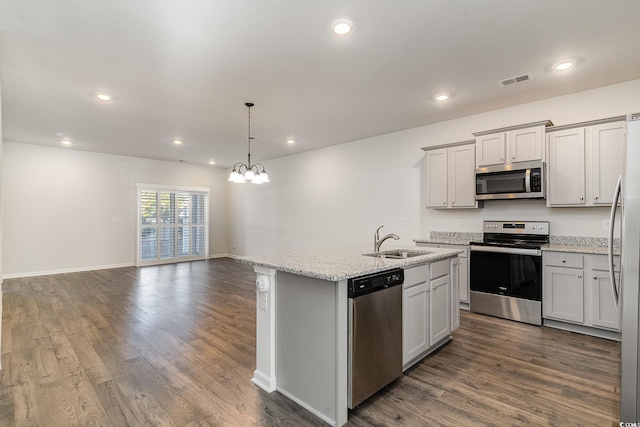 kitchen with light stone countertops, appliances with stainless steel finishes, sink, pendant lighting, and an island with sink