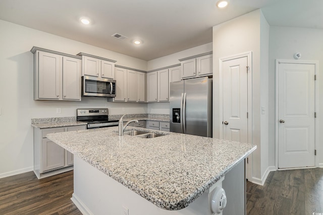 kitchen featuring light stone countertops, sink, stainless steel appliances, dark hardwood / wood-style flooring, and a center island with sink