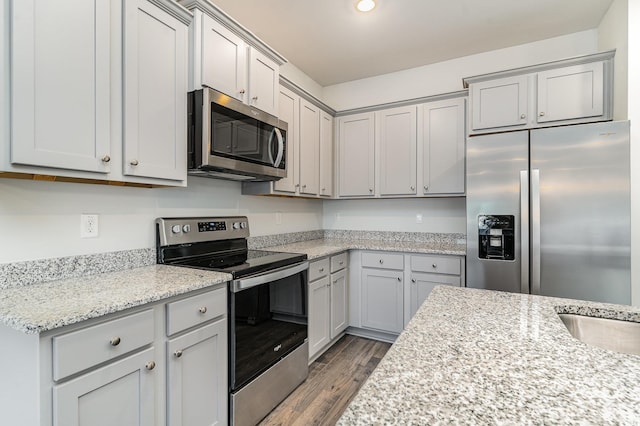 kitchen with hardwood / wood-style floors, gray cabinets, light stone counters, and appliances with stainless steel finishes