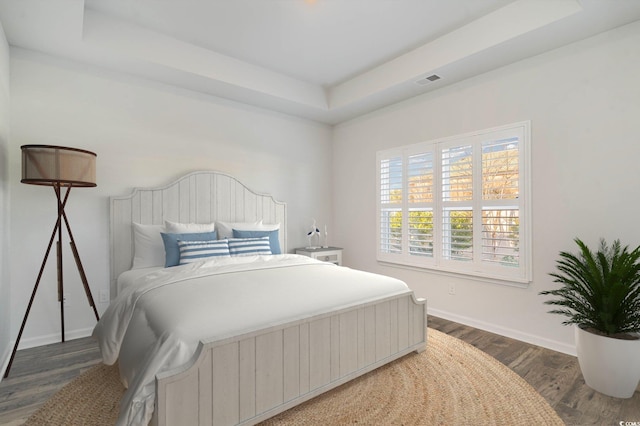 bedroom with dark hardwood / wood-style floors and a raised ceiling