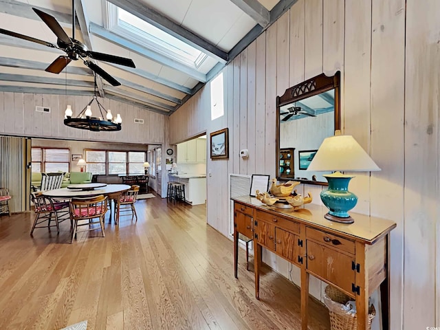 dining area with beamed ceiling, light hardwood / wood-style floors, wood walls, and a skylight