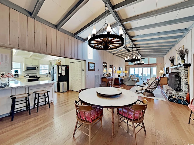 dining space featuring a chandelier, beam ceiling, a brick fireplace, and a wealth of natural light