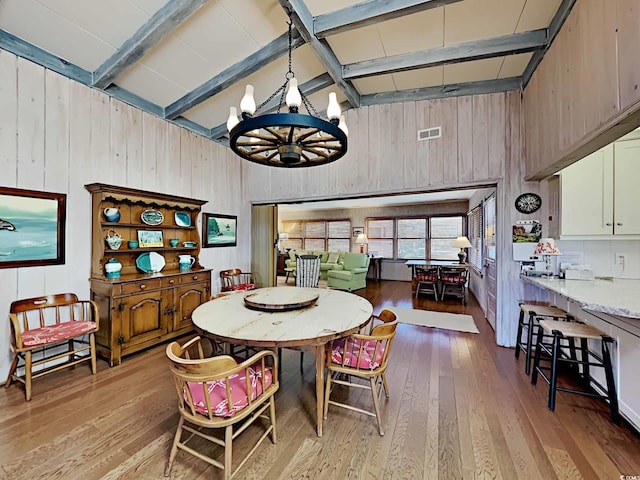 dining area featuring wood walls, high vaulted ceiling, light hardwood / wood-style floors, a notable chandelier, and beam ceiling