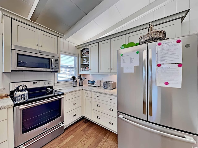 kitchen with light stone counters, wood-type flooring, vaulted ceiling, gray cabinets, and appliances with stainless steel finishes