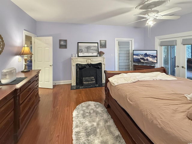 bedroom featuring ceiling fan, wood-type flooring, a fireplace, and french doors