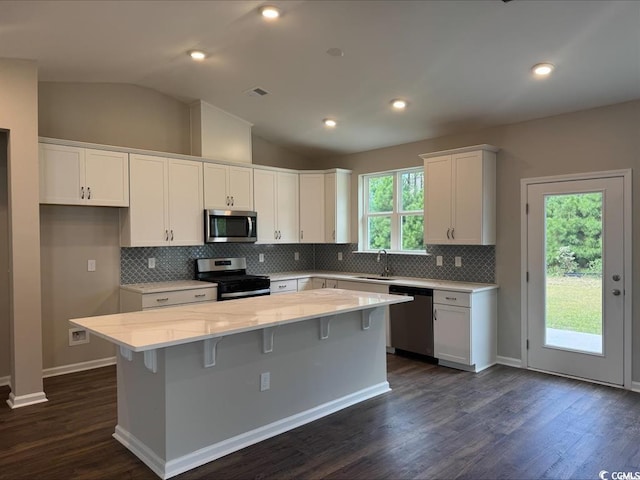 kitchen with lofted ceiling, sink, appliances with stainless steel finishes, white cabinetry, and a kitchen island