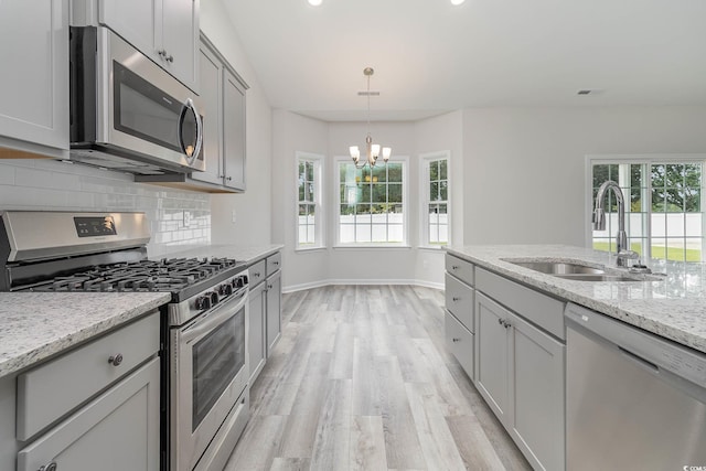 kitchen with gray cabinetry, light stone countertops, sink, a chandelier, and appliances with stainless steel finishes