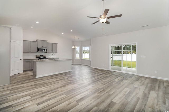 unfurnished living room with ceiling fan with notable chandelier, light hardwood / wood-style floors, and plenty of natural light