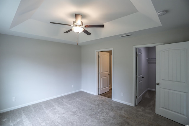 unfurnished bedroom with a walk in closet, dark carpet, a raised ceiling, ceiling fan, and a closet