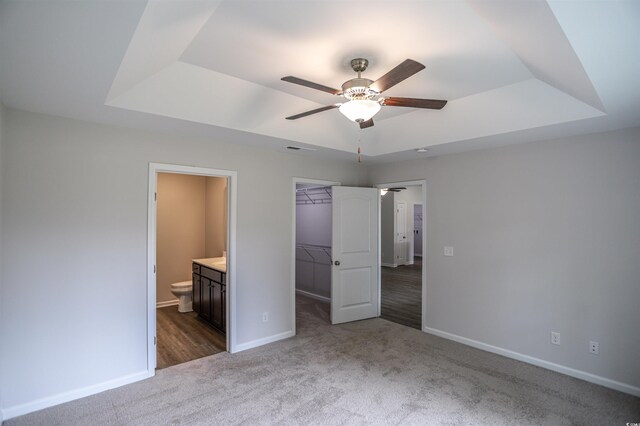 unfurnished bedroom featuring ensuite bathroom, a closet, a walk in closet, and a tray ceiling