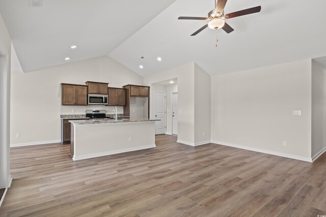 kitchen featuring a center island with sink, sink, vaulted ceiling, light wood-type flooring, and appliances with stainless steel finishes