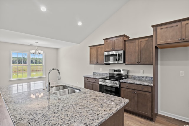 kitchen with appliances with stainless steel finishes, sink, pendant lighting, a center island with sink, and a notable chandelier