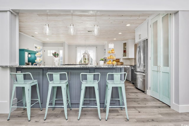 kitchen featuring pendant lighting, white cabinetry, stainless steel refrigerator, and a kitchen breakfast bar