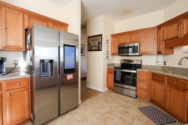 kitchen featuring sink, appliances with stainless steel finishes, light tile patterned flooring, and a textured ceiling