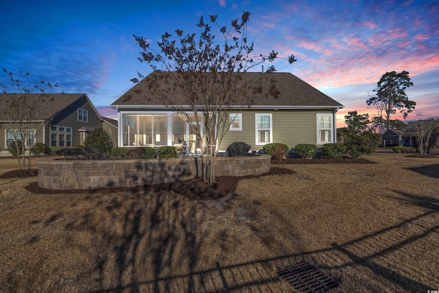 back house at dusk with a yard and a sunroom