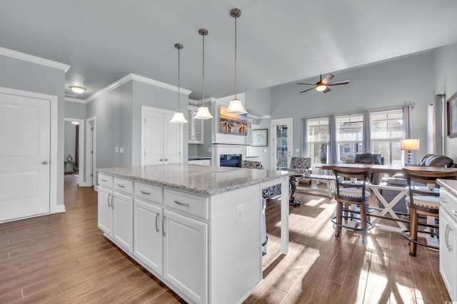 kitchen featuring light stone countertops, ceiling fan, decorative light fixtures, white cabinets, and a center island