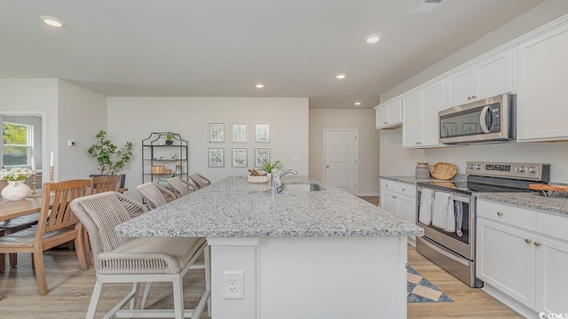 kitchen featuring stainless steel appliances, sink, light stone counters, a kitchen breakfast bar, and a kitchen island with sink