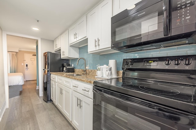 kitchen with a sink, black appliances, light wood-style flooring, and white cabinets