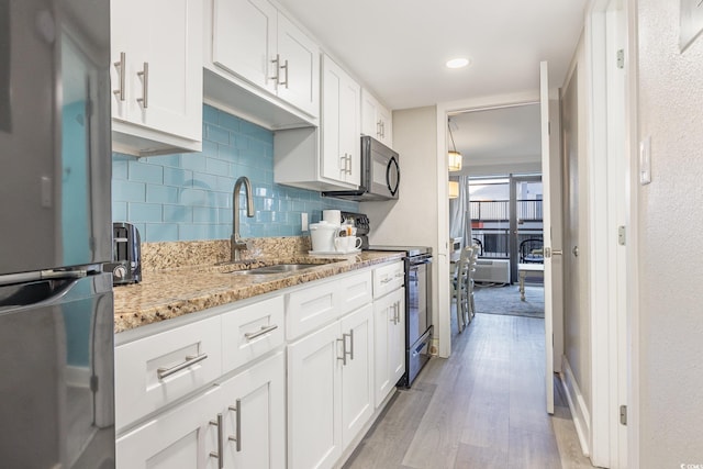 kitchen featuring light stone countertops, sink, white cabinetry, and black appliances