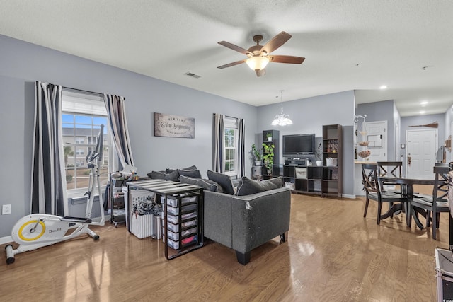 living room featuring hardwood / wood-style floors, ceiling fan with notable chandelier, and a textured ceiling