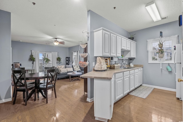 kitchen featuring white cabinets, light wood-type flooring, ceiling fan, and sink