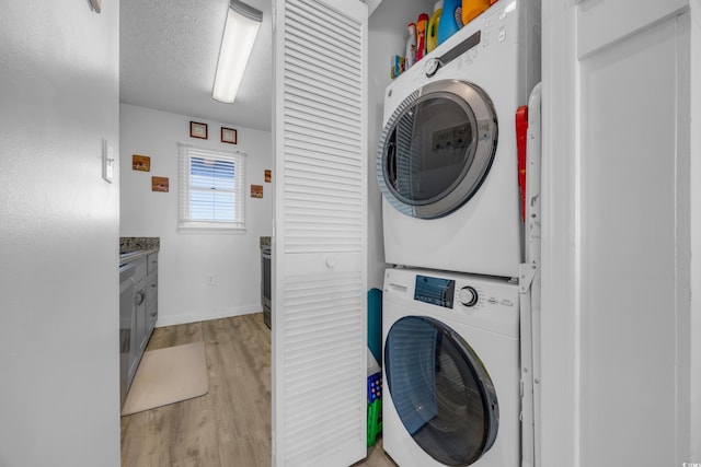 clothes washing area featuring a textured ceiling, light hardwood / wood-style floors, and stacked washer / drying machine