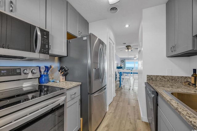 kitchen with ceiling fan, gray cabinets, light stone countertops, and stainless steel appliances