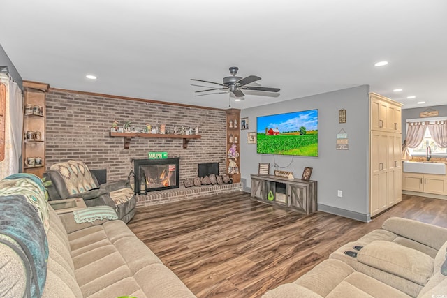 living room featuring ceiling fan, sink, dark wood-type flooring, and a brick fireplace