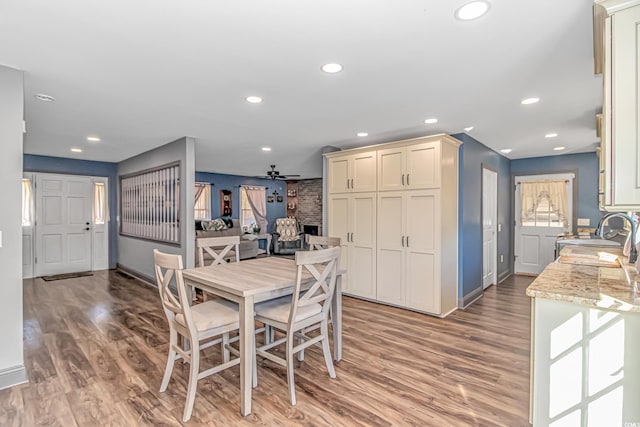 dining area featuring ceiling fan, wood-type flooring, sink, and a brick fireplace