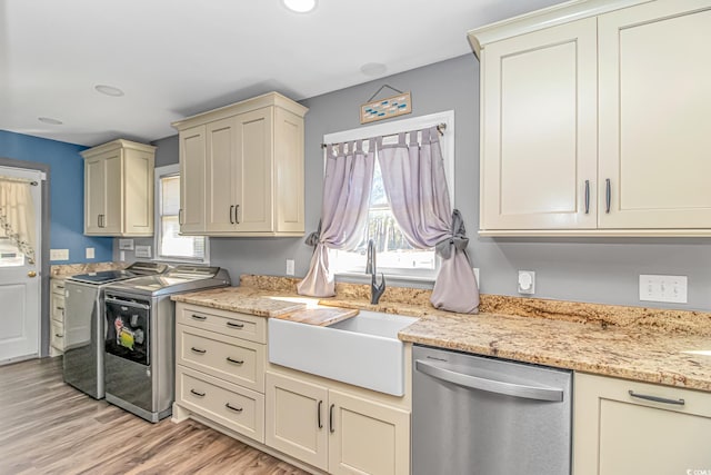 kitchen featuring stainless steel dishwasher, sink, washer and dryer, cream cabinetry, and light hardwood / wood-style floors