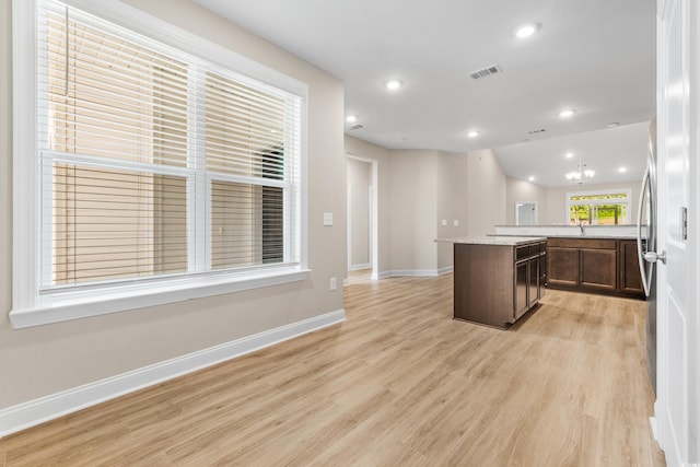 kitchen featuring vaulted ceiling, a kitchen island, sink, light stone countertops, and light wood-type flooring