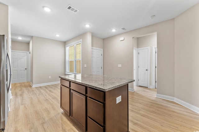 kitchen with dark brown cabinets, light wood-type flooring, stainless steel refrigerator, a kitchen island, and light stone countertops