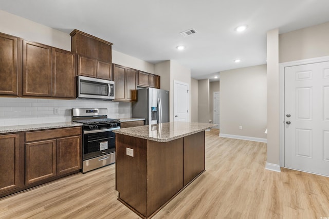 kitchen with a kitchen island, appliances with stainless steel finishes, tasteful backsplash, light stone counters, and light hardwood / wood-style flooring