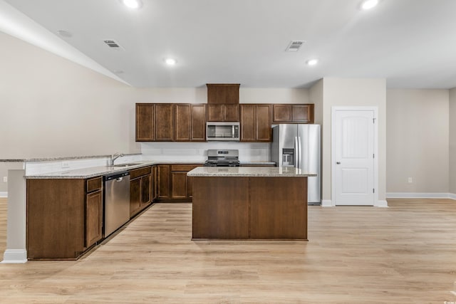 kitchen featuring sink, stainless steel appliances, light stone counters, light hardwood / wood-style floors, and a kitchen island