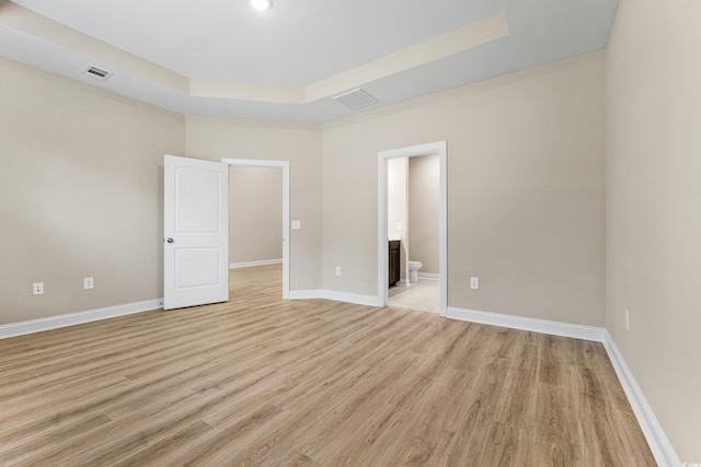 empty room featuring a tray ceiling and light wood-type flooring