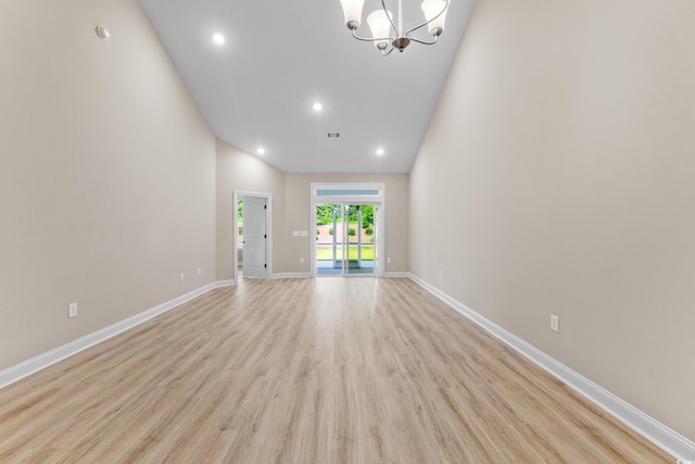 unfurnished living room with light wood-type flooring, a notable chandelier, and high vaulted ceiling