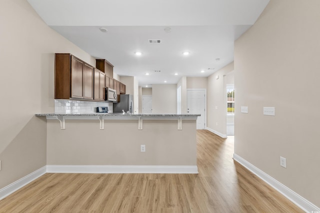 kitchen with stainless steel appliances, light stone countertops, a kitchen bar, decorative backsplash, and kitchen peninsula