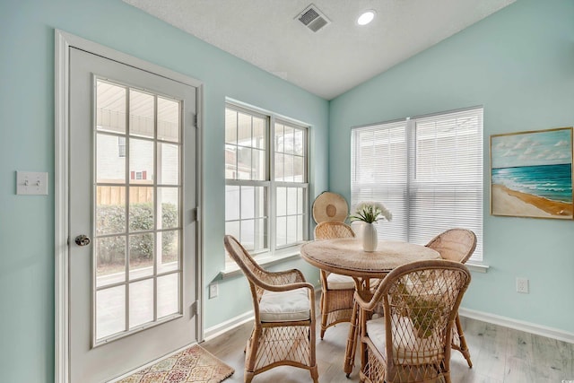 dining area with a textured ceiling, light hardwood / wood-style floors, and vaulted ceiling